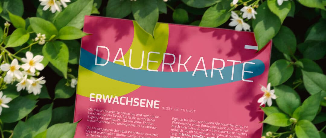Pinke Dauerkarte für Erwachsene der Landesgartenschau zwischen grünen Blättern und weißen Blüten