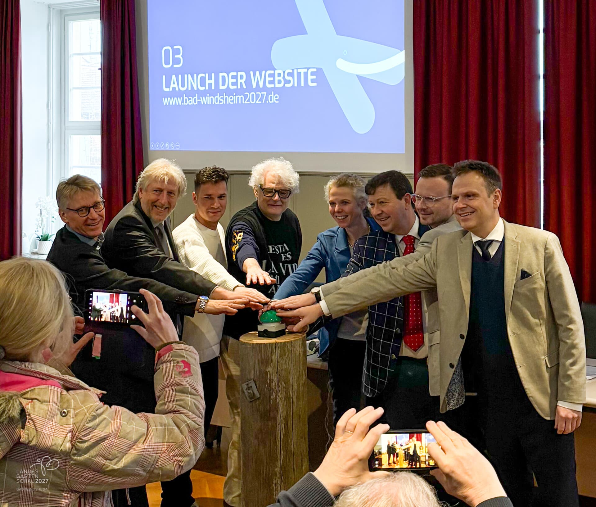 Gruppe drückt gemeinsam einen grünen Buzzer, auf der Leinwand steht „Launch der Website“