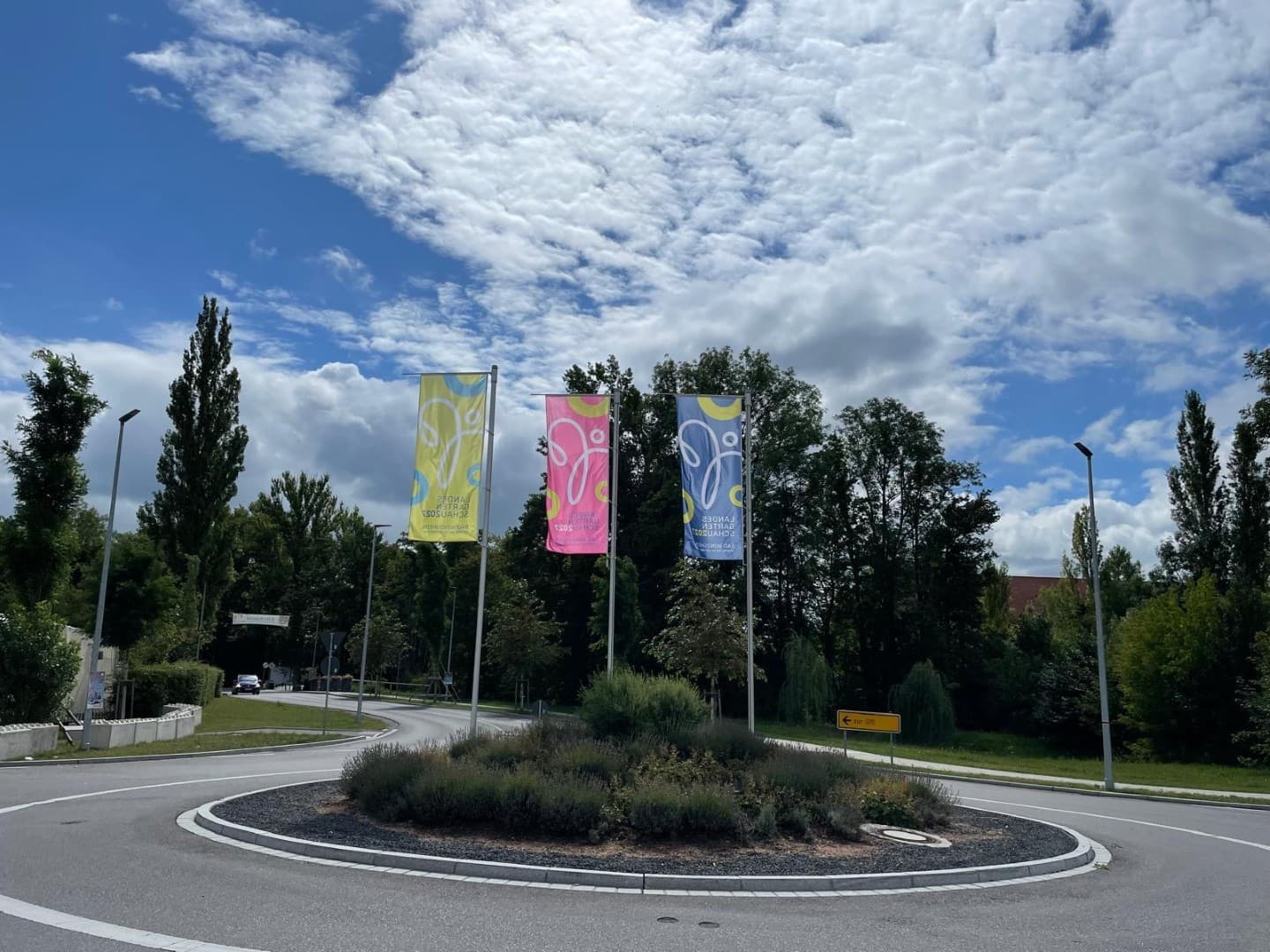 Drei Landesgartenschau-Fahnen in Gelb, Pink und Blau an einem Kreisverkehr