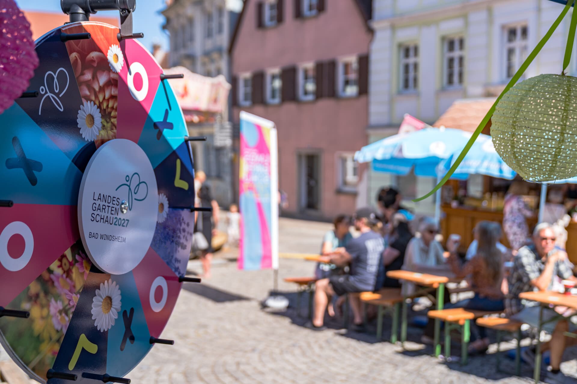 Glücksrad der Landesgartenschau auf dem Altstadtfest, dahinter Besucher an Biertischgarnituren