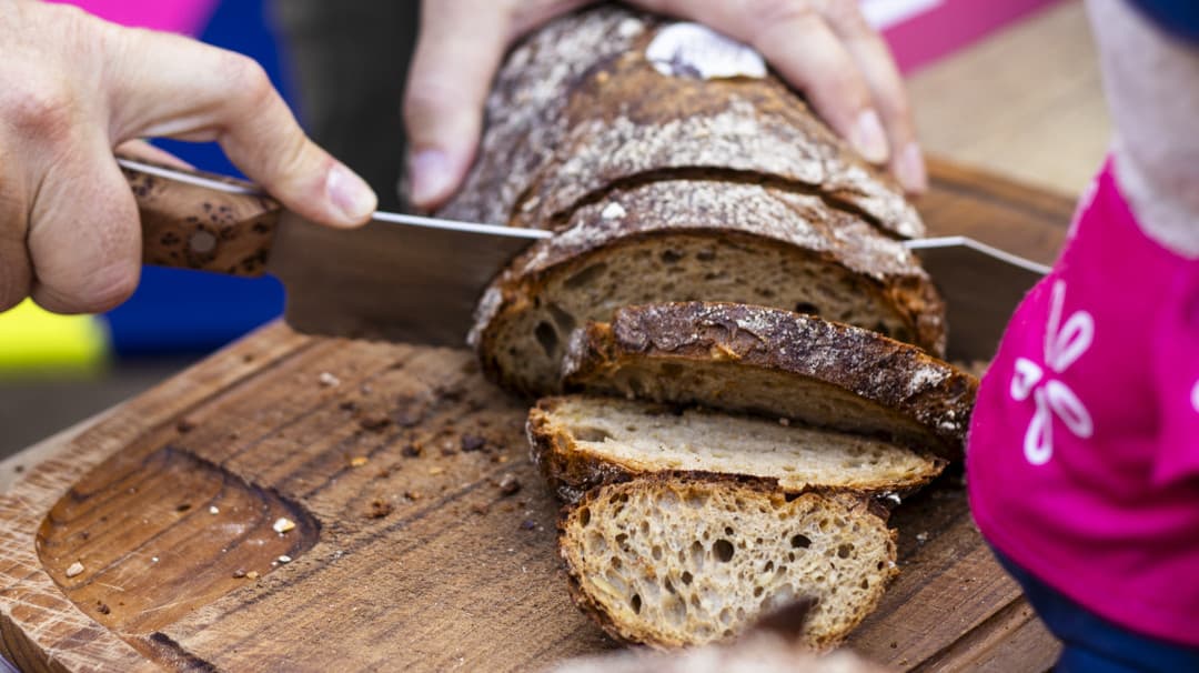 Hände schneiden das Landesgartenschau-Brot auf einem Holzbrett auf