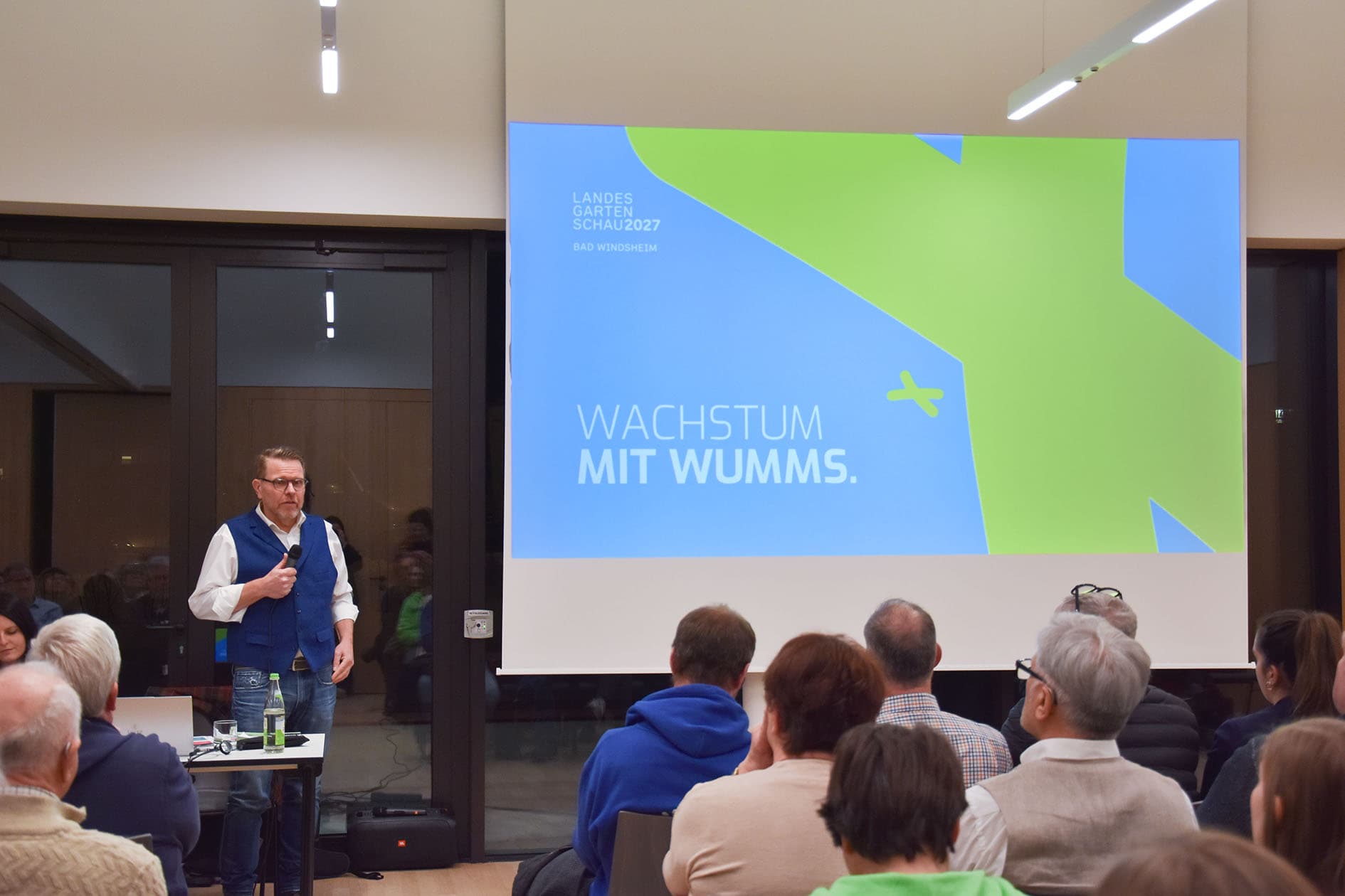 Referent vor einer Leinwand mit dem Schriftzug „Wachstum mit Wumms“ vor vollem Saal