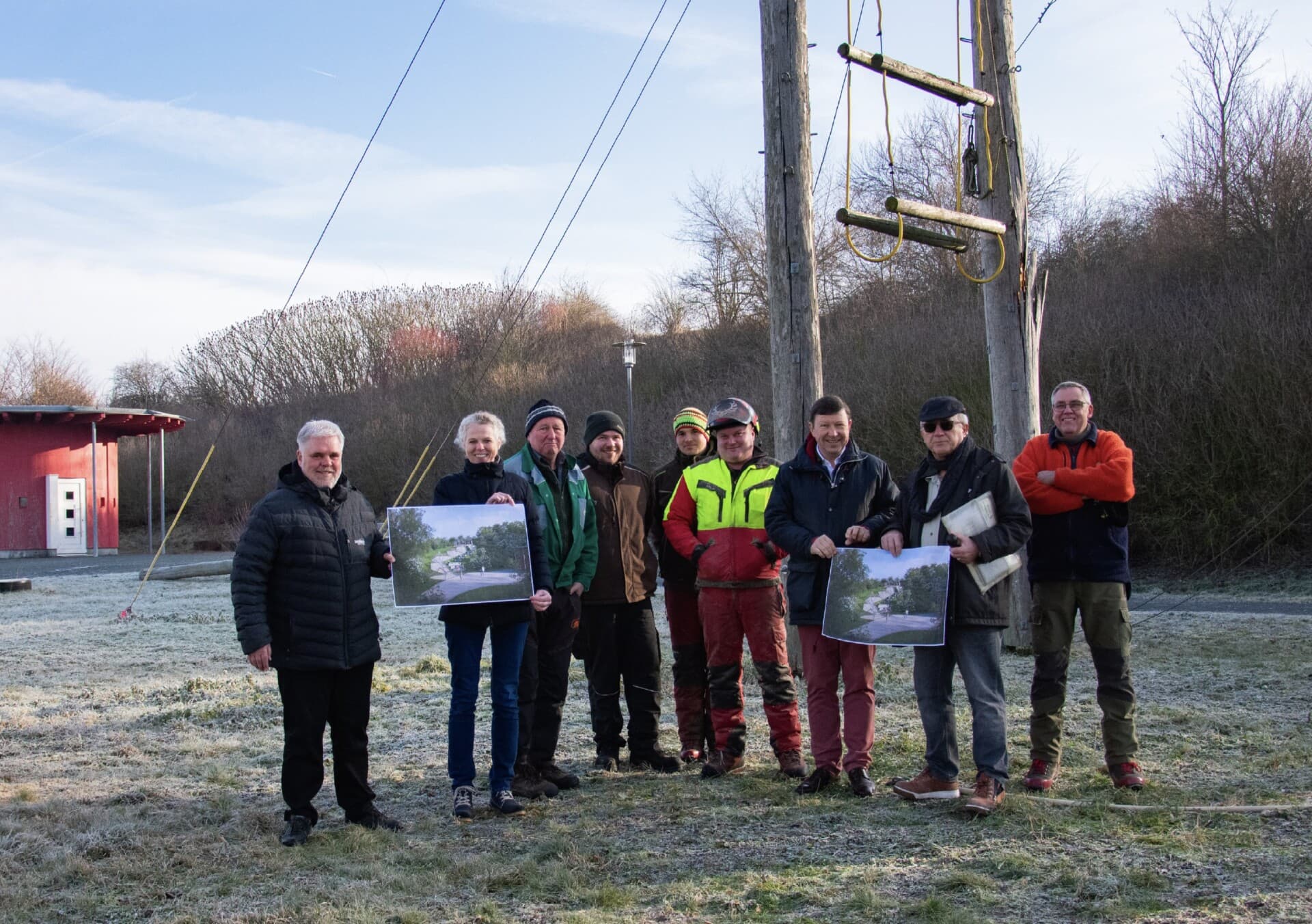 Gruppe mit gerahmten Planbildern vor einem Mast des Hochseilgartens bei Raureif