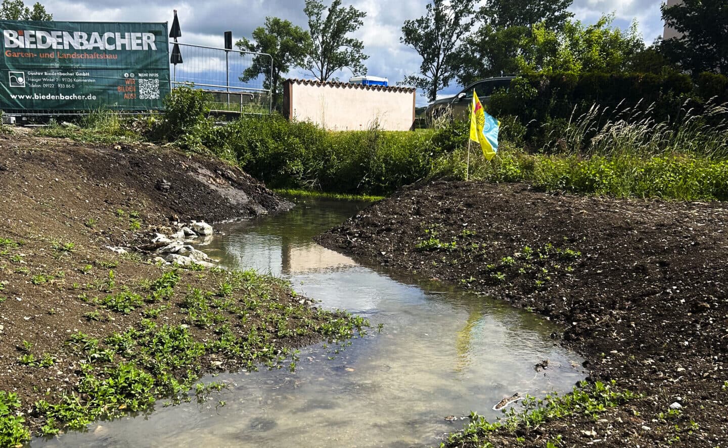 Wasser fließt durch das frisch angelegte Bachbett des Kühwasengrabens zwischen aufgeschütteten Erdwällen