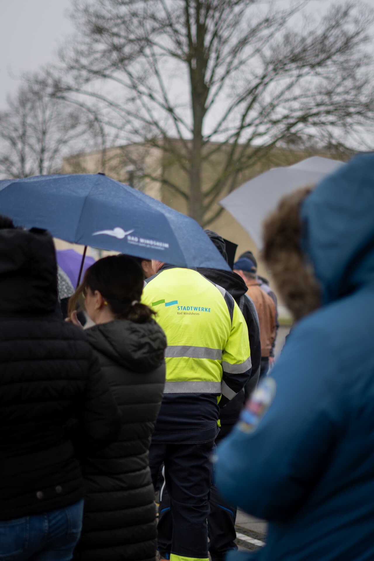 Menschen mit Regenschirmen bei einer Veranstaltung im Freien, vorne ein Mitarbeiter der Stadtwerke in Warnweste