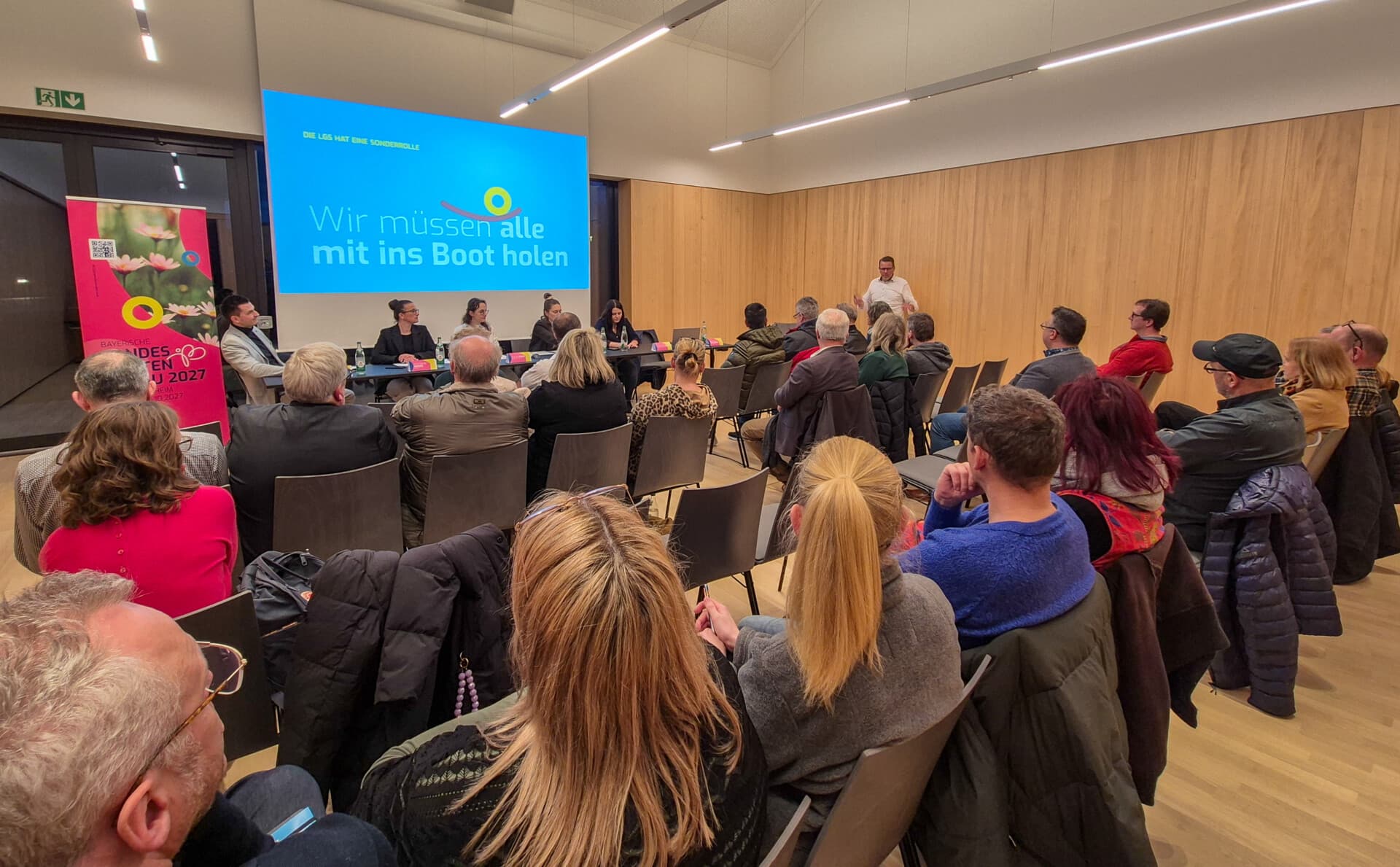 Besetzter Saal beim Unternehmerabend, auf der Leinwand der Satz „Wir müssen alle mit ins Boot holen“